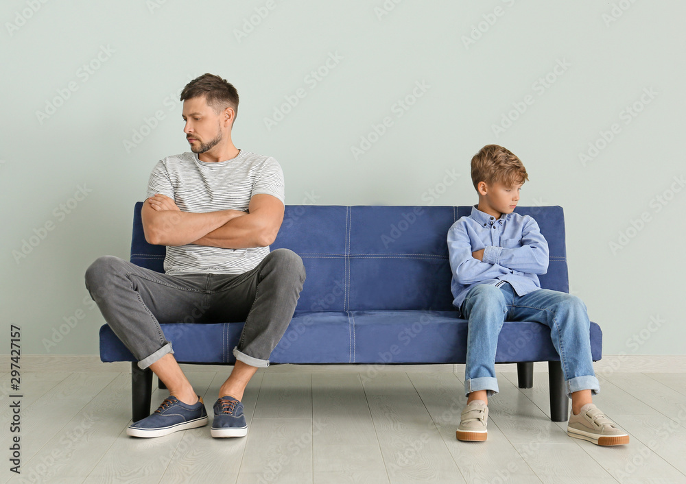 Quarreled father and son sitting on sofa at home Quarreled father and son sitting on sofa at home