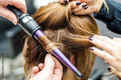 Professional hairdresser is twisting the hair with a curling iron in beauty salon close up. Concept female stylist.