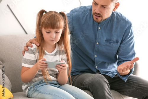 Little girl with mobile phone ignoring her angry father at home