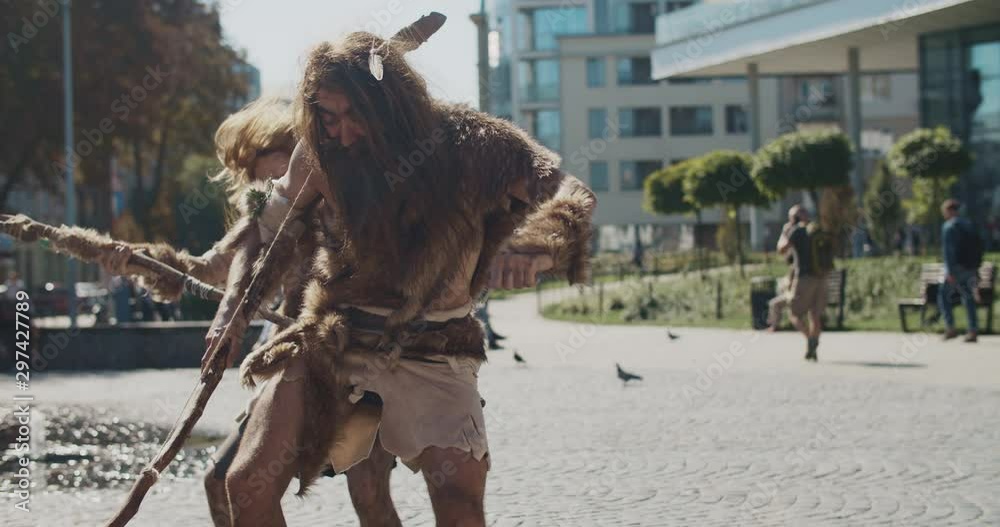 Funny neanderthals man of hunter-gatherers in animal fur holding prehistoric weapon dancing hunting animals in modern city look around wonder timetraveler evolution caveman civilization slow motion Funny neanderthals man of hunter-gatherers in animal fur holding prehistoric weapon dancing hunting animals in modern city look around wonder timetraveler evolution caveman civilization slow motion