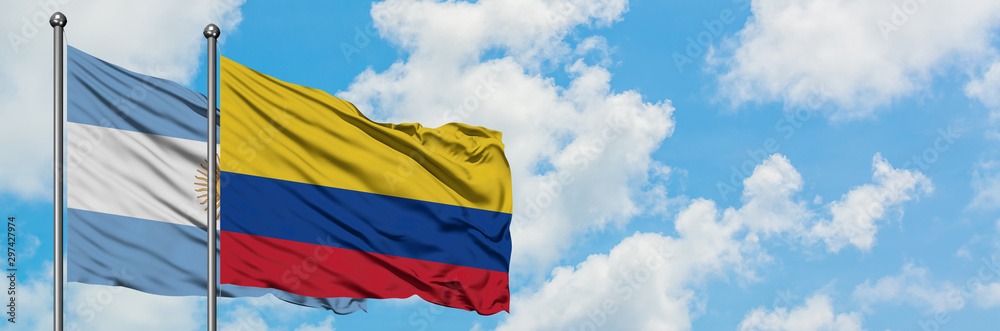 Fototapeta premium Argentina and Colombia flag waving in the wind against white cloudy blue sky together. Diplomacy concept, international relations.