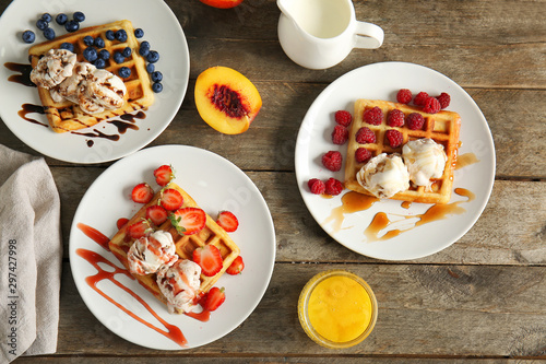 Plates with tasty waffles, berries and ice cream on table