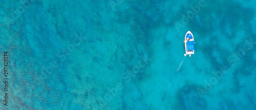 An aerial view of a boat in  the beautiful Mediterranean sea, where you can se the rocky textured underwater corals and the clean turquoise water of blue lagoon Agia Napa