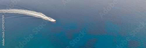 An aerial view of a boat speeding in the beautiful Mediterranean sea, where you can se the rocky textured underwater corals and the clean turquoise water of blue lagoon Agia Napa