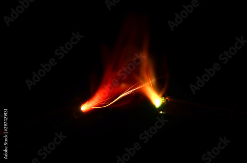 Colored sparks mainly with red and green nuances seen between two impregnated electrodes on a dark background
