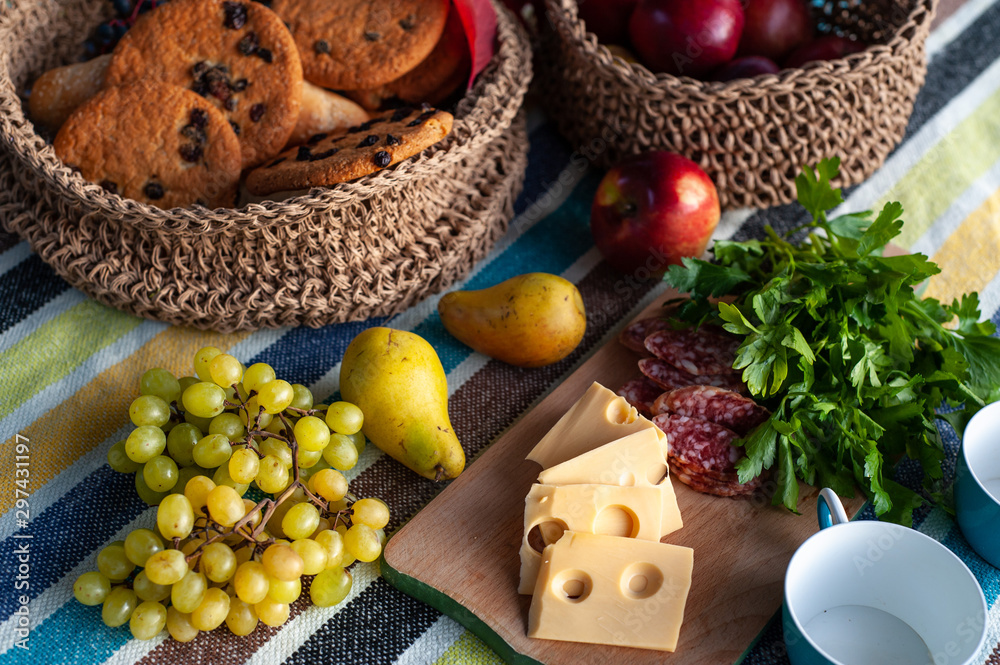 view from above of a table with fruits and cookies in wicker baskets and sliced cheese, sausage and a bunch of greenery