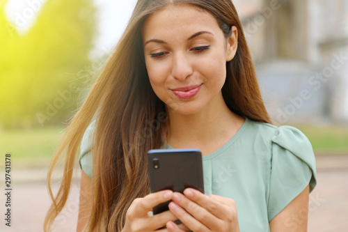 Close up of beautiful smiling woman typing on smart phone outdoor.
