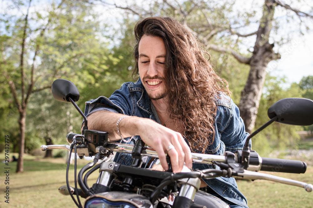 Joven motociclista sonriente de pelo largo en el parque 