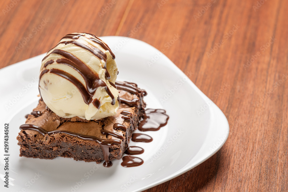 Chocolate Brownie with Vanilla Ice Cream and chocolatel syrup isolated on wooden background Chocolate Brownie with Vanilla Ice Cream and chocolatel syrup isolated on wooden background