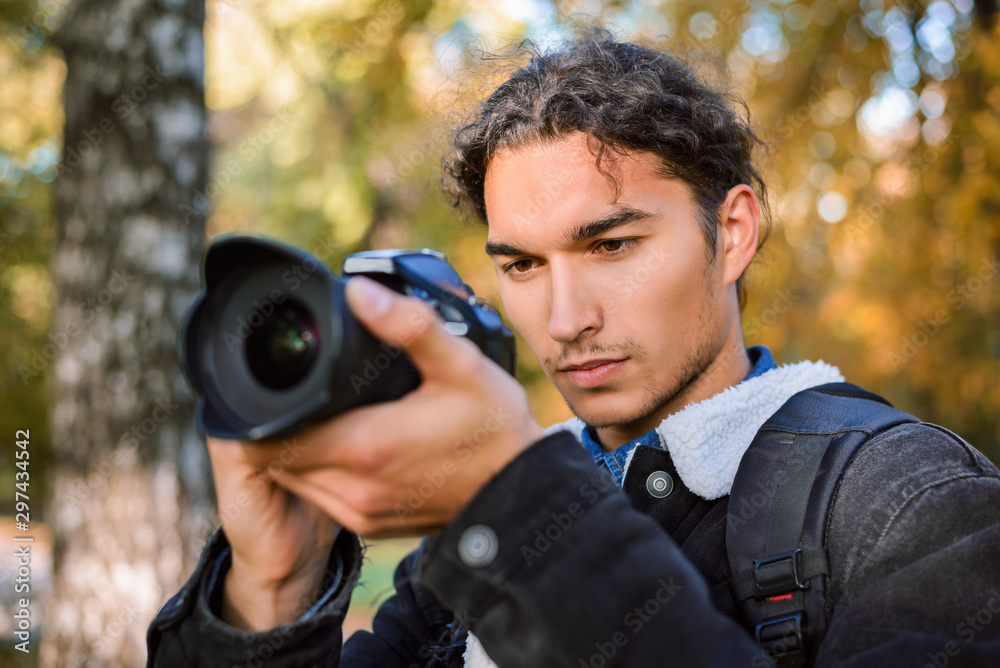 Young male photographer photographing nature. Consentrated student photographer shooting autumn landscape in forest in the morning