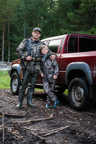 Father and son came to the forest for hunting together. Standing with a shotgun rifle in front of pickup truck.
