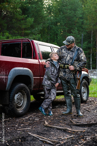 Happy hunter with his son near their pickup truck before hunting in a forest