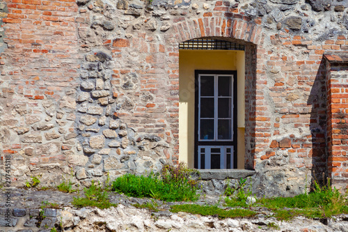 A fragment of an old fortress wall with an opening for a door through which the wall and door of a modern building are visible. A symbol of the connection of the past and the present © igor_zubkov