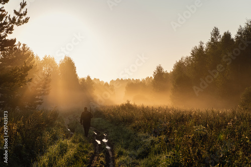 Bird Hunter at Sunrise going for hunt in a forest with his shotgun rifle.