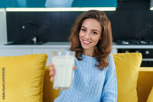 Canvas Print Smiling woman gives to the camera a glass of fresh milk in the stylish cozy kitchen at the morning