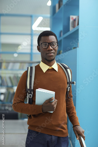 Waist up portrait of smart African-American student holding book standing in college library