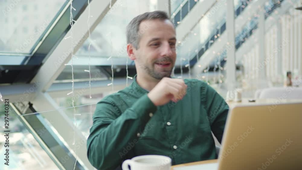 Camera panning right to glad adult entrepreneur using laptop then leaning back on chair and looking away while working on project in cafe