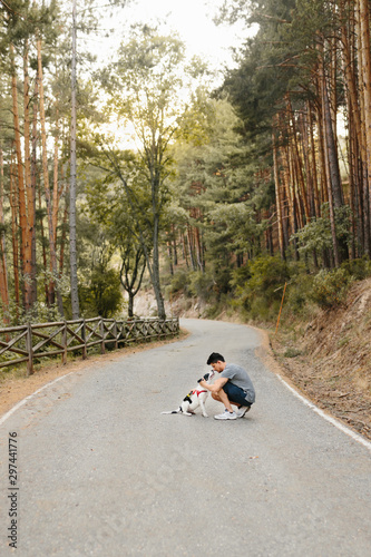 Alone man kissing, hugging and caressing her family member black and white labrador dog on the road in the pine forest under the evening sunlight