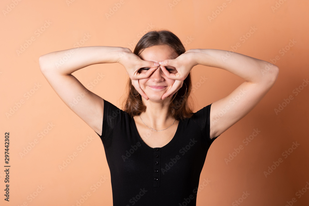 Girl makes glasses with hands, on a light orange background. Girl makes glasses with hands, on a light orange background.