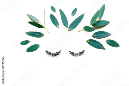 Female face made of false eyelashes and eucalyptus leaves  on white background