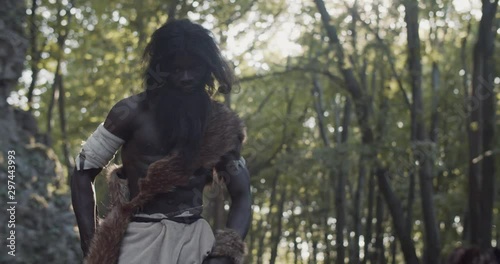 Portrait of black caveman holding weapon neanderthals wearing animal skin stand dance look around in prehistoric forest ancient bushman aboriginal evolution stone primitive cave slow motion