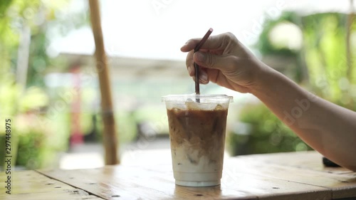 Hand mixing coffee with milk for making iced latte drink with the straw