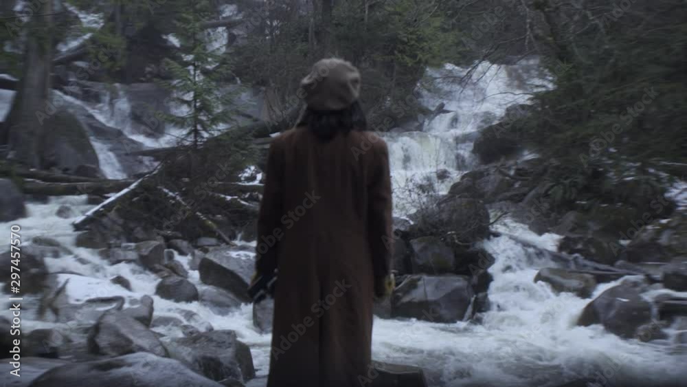 A young woman admires a swift mountain river running through a forest. A young woman admires a swift mountain river running through a forest.