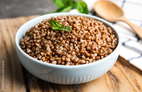 Bowl of buckwheat porridge with basil on wooden board