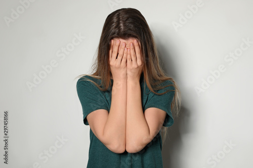Upset young woman crying against light background © New Africa