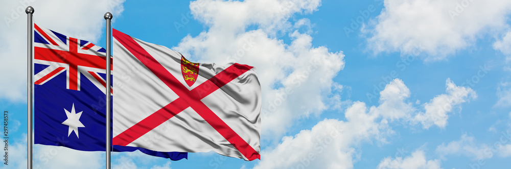 Australia and Jersey flag waving in the wind against white cloudy blue sky together. Diplomacy concept, international relations. Australia and Jersey flag waving in the wind against white cloudy blue sky together. Diplomacy concept, international relations.