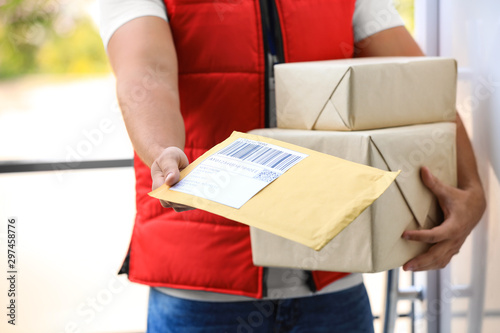 Young courier holding parcels on doorstep, closeup. Delivery service