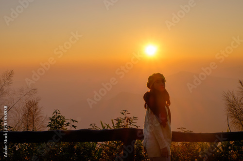 Woman tourist is a cheerfully, she is watching sunrise with mist in the morning, orange sky, viewpoint at Phu Ruea National Park, Loei, Thailand. photo