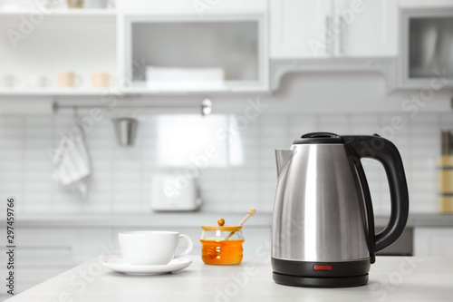 Modern electric kettle, cup and honey on wooden table in kitchen photo