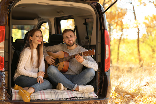 Young couple with guitar sitting in open car trunk outdoors © New Africa