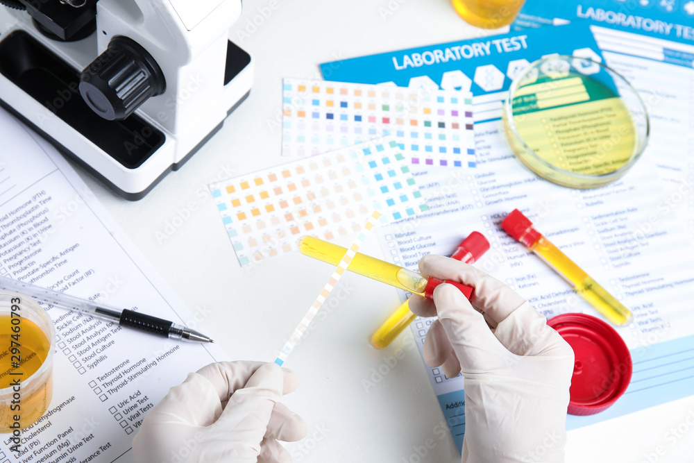 Fototapeta premium Doctor holding test tube with urine sample for analysis at white table, top view