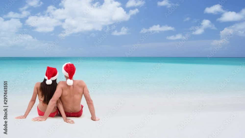 CINEMAGRAPH - seamless loop: Christmas couple sitting down relaxing on white sand beach sunbathing in tropical travel destination in winter holidays. Young adults wearing santa hat looking at view. CINEMAGRAPH - seamless loop: Christmas couple sitting down relaxing on white sand beach sunbathing in tropical travel destination in winter holidays. Young adults wearing santa hat looking at view.