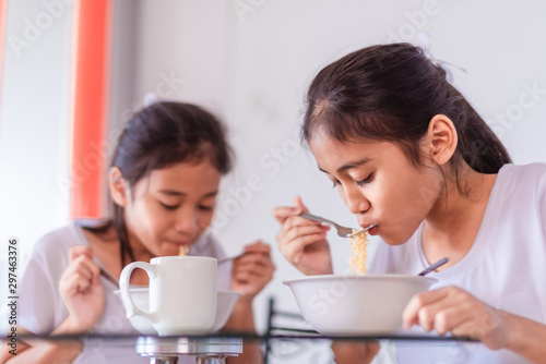 The old sister and the young sister are eating yellow noodles in the white bowls. It's delicious but spicy. Both of them wore a white T-shirt with a smiling face. The white background is behind them.