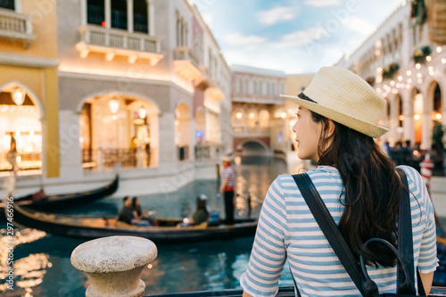 Canvas Print back view of elegant woman traveler with sunhat enjoy view to canal with passing by gondola in las vegas famous hotel