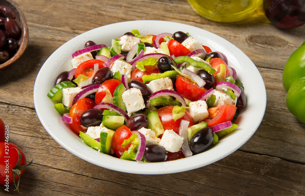  Traditional Greek salad in a round white bowl on an old rustic wooden table. Selected focus.