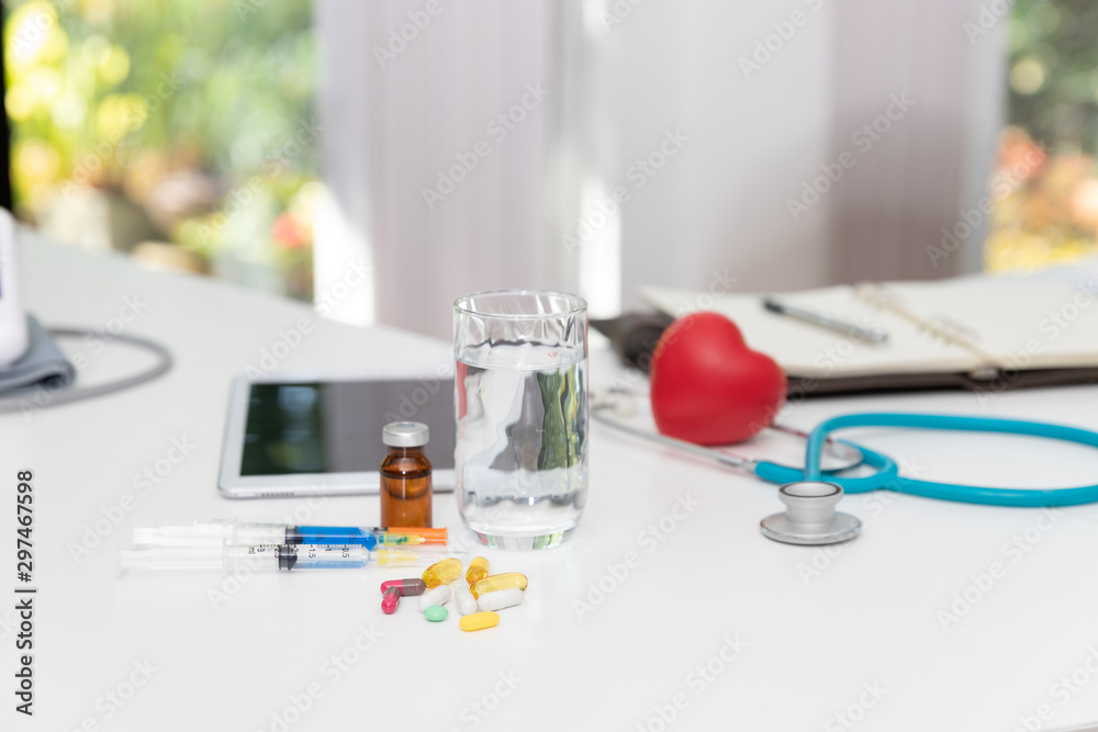 Close up assorted pharmaceutical medicine pills,injection needle,glass of water and vaccine on table