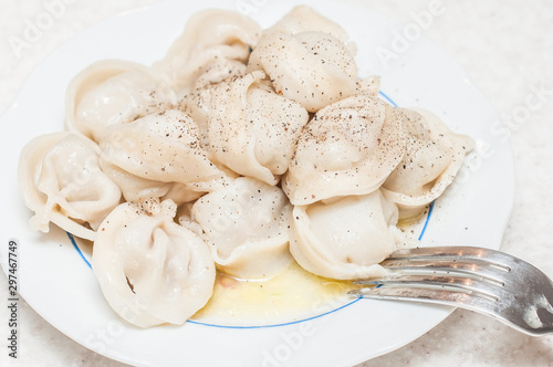 A small portion of freshly cooked dumplings with butter sprinkled with pepper on a white plate with a fork.