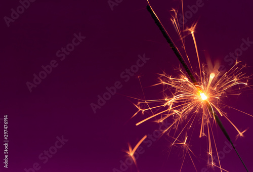Burning christmas sparkler on purple background with room for text