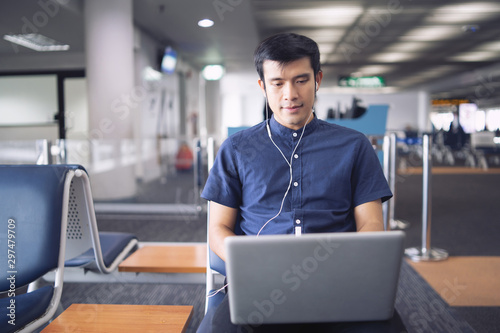 Businessman sitting at the airport working with laptop waiting for his flight with a suitcase, He online banking on the internet for business travel, shopping, and payment on traveling concept.