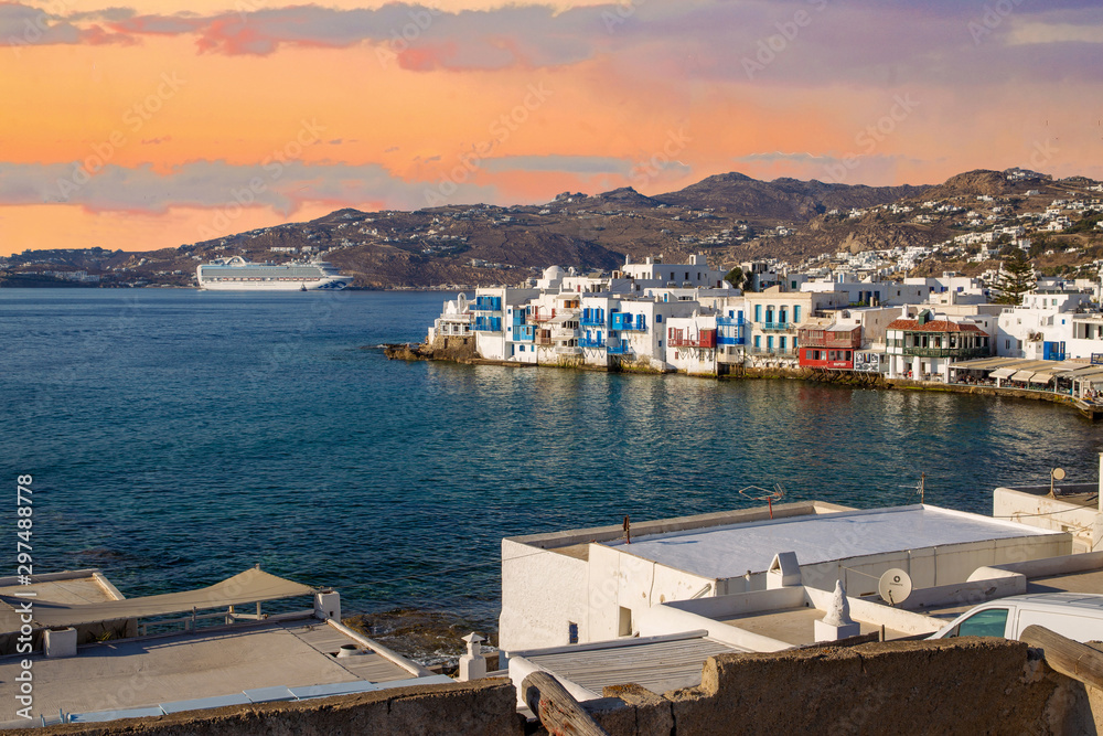 Idyllic   morning  on greek island  Mykonos! View on  smallwhite houses  andyou at distant large ocean liner at new harbor . Some people go  to sleep after party in night club.