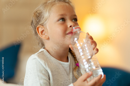 Little pretty girl drinks water and holds plastic bottle in her hands.