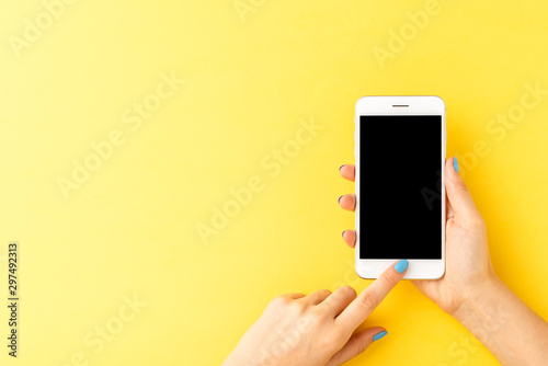 Woman’s hands using mobile phone with empty screen on yellow background. Top view photo