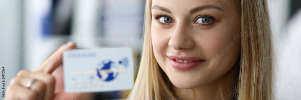 Focus on trendy businesswoman wearing striped blouse. Tender hand of attractive woman holding white business bank card and smiling at camera with joy and gladness. Blurred background Focus on trendy businesswoman wearing striped blouse. Tender hand of attractive woman holding white business bank card and smiling at camera with joy and gladness. Blurred background