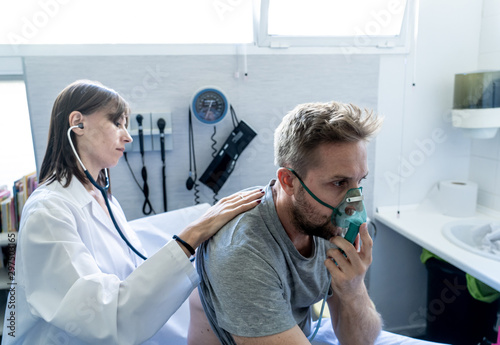 Sick man Inhaling Through Oxygen Mask having a medical exam by female doctor at hospital