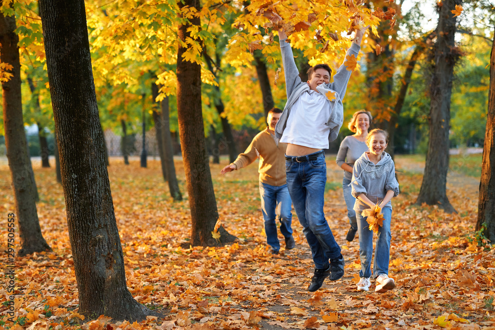 Happy family having holiday in autumn city park. Children and parents running, smiling, playing and having fun. Bright yellow trees and leaves Happy family having holiday in autumn city park. Children and parents running, smiling, playing and having fun. Bright yellow trees and leaves