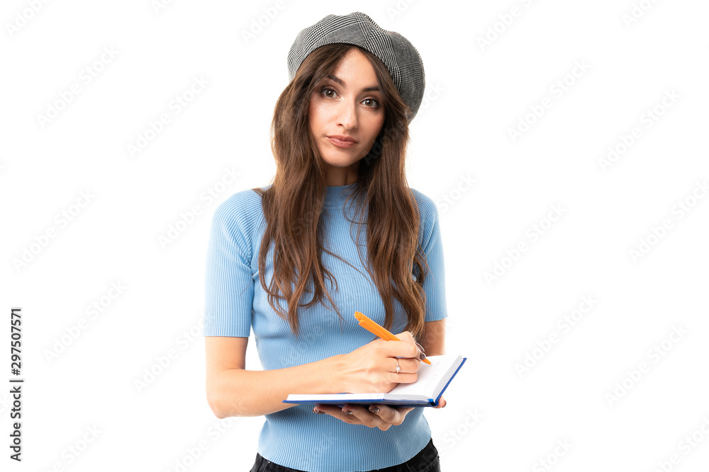 Young girl with delightful smile, long wavy chestnut hair, beautiful makeup, in blue jersey, black jeans, grey beret, standing with notebook and pen Young girl with delightful smile, long wavy chestnut hair, beautiful makeup, in blue jersey, black jeans, grey beret, standing with notebook and pen
